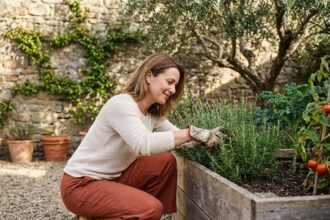 Femme aménageant un potager surélevé dans un jardin bordelais avec mur en pierre et chemin en gravier